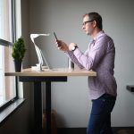 Person standing at a Nimbus desk beside a window