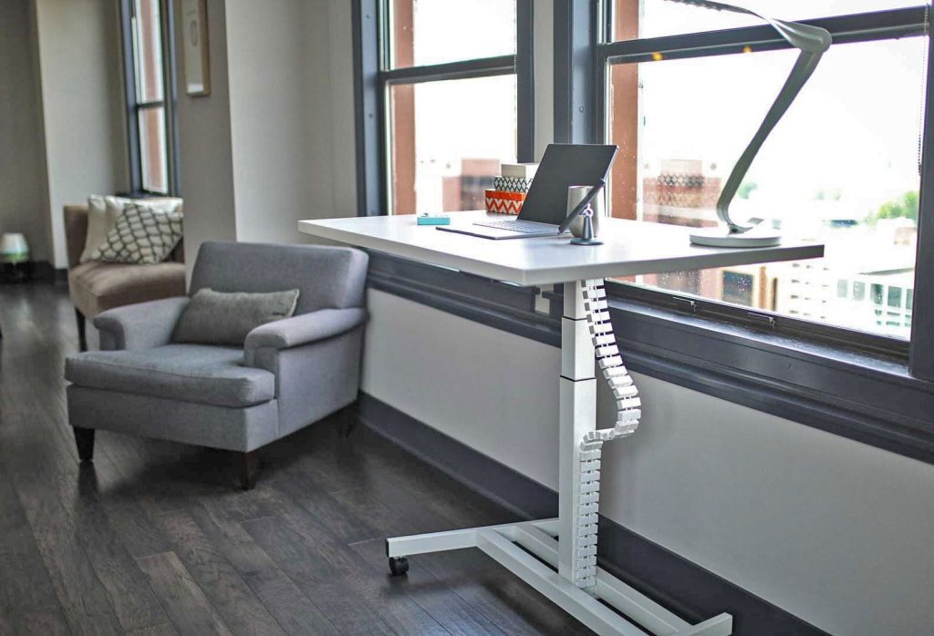 Height-adjustable desk with an articulated white cable carrier along one leg