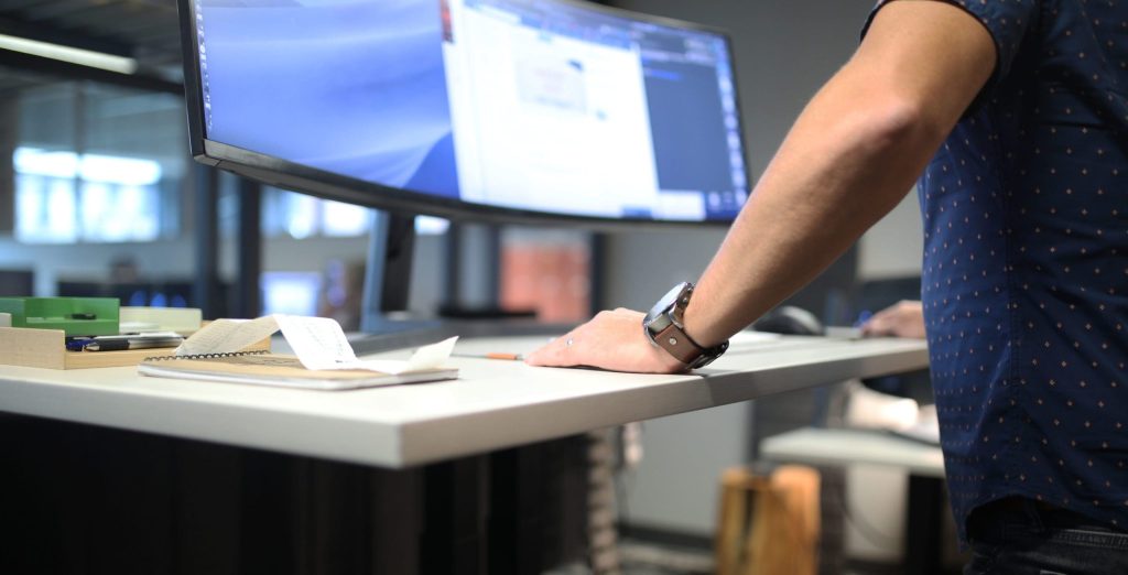 Person at a height-adjustable desk with a monitor and work accessories