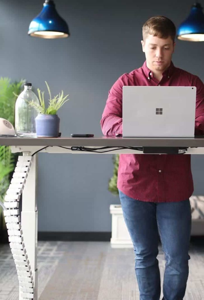 Person at an adjustable desk with a white cable carrier along the frame