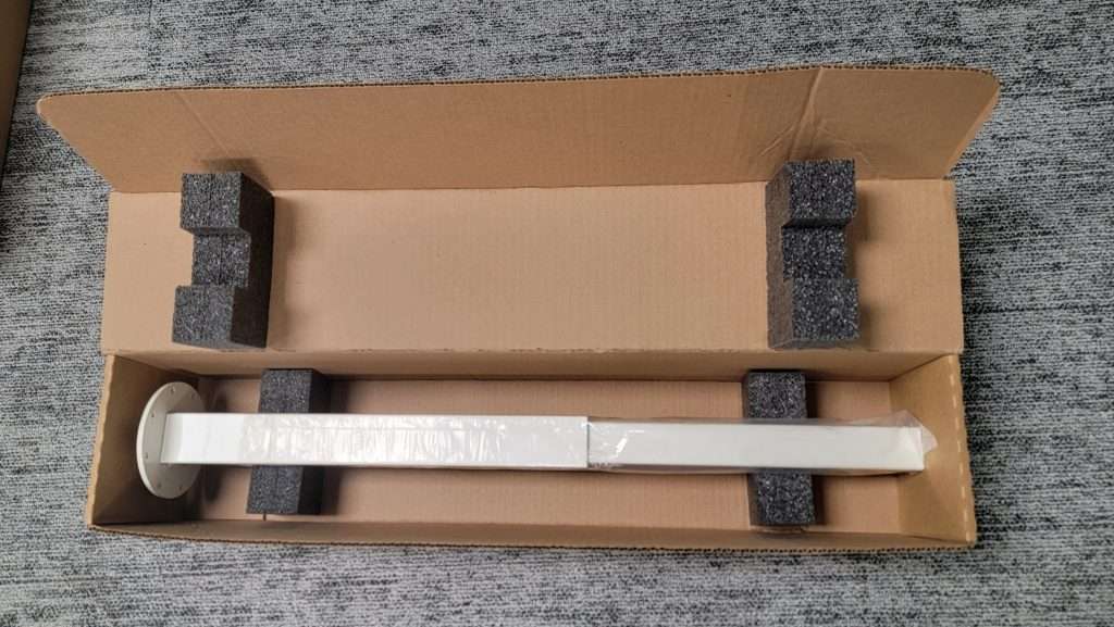 A white desk frame component packed in a cardboard shipping carton.