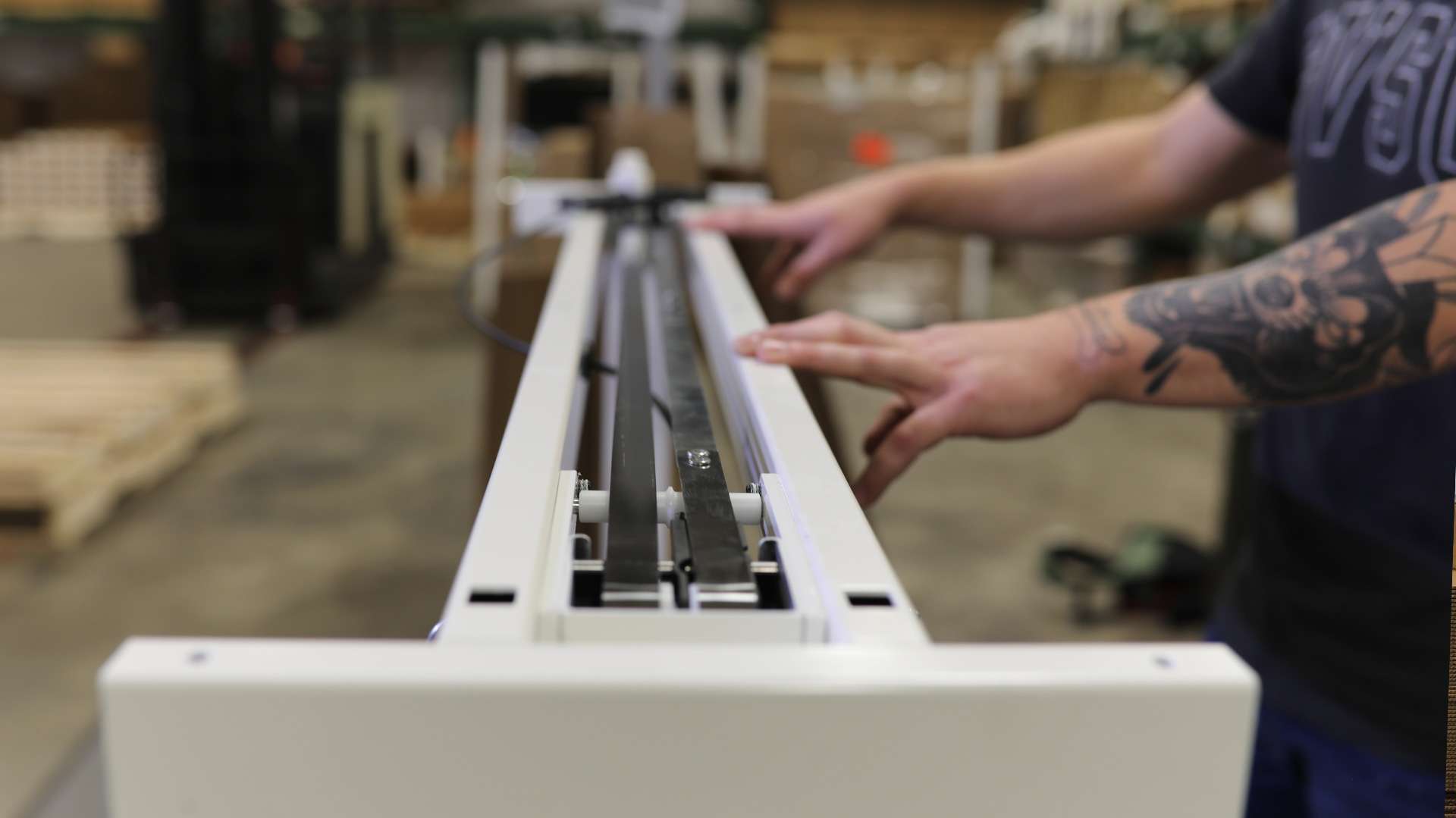 A technician assembles a white standing desk frame in the workshop.